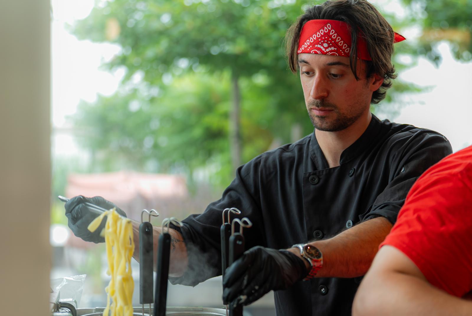 Chef lifting freshly cooked pasta at a Pastasole catering station
