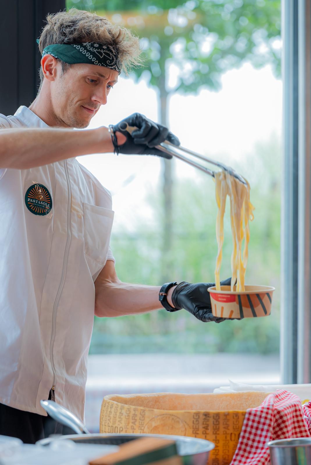 Chef serving fresh pasta from the Parmesan wheel at a Pastasole catering event